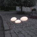 Solarne lampy ogrodowe LED w kształcie kamieni świecące ciepłym światłem ustawione na żwirowej rabacie przy ścieżce ogrodowej. Dekoracyjne oświetlenie solarne do ogrodu, na podjazd, rabaty i przy domu.