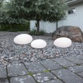 Trzy lampy solarne LED w formie kamieni ustawione na żwirowej rabacie w ogrodzie przy dużym głazie i drzewie. Dekoracyjne oświetlenie solarne do ogrodu i wokół domu.