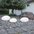 Trzy lampy solarne LED w formie kamieni ustawione na żwirowej rabacie w ogrodzie przy dużym głazie i drzewie. Dekoracyjne oświetlenie solarne do ogrodu i wokół domu.