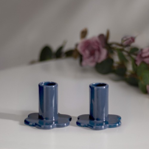 Dwa niebieskie porcelanowe świeczniki Bloom ustawione na jasnej powierzchni z delikatnie rozmytym tłem kwiatowym.