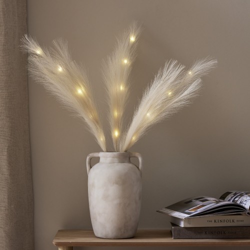 Dekoracyjne pióra LED w kolorze ecru z ciepłym światłem, umieszczone w wazonie na drewnianej konsoli w jasnym wnętrzu.