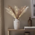 Dekoracyjne pióra LED w kolorze ecru i brązowym w ceramicznym wazonie na drewnianej półce tworzą elegancką aranżację wnętrza z ciepłym światłem.