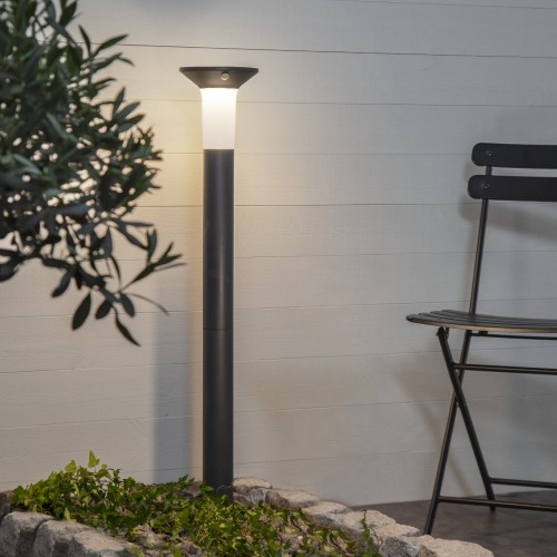 Solarna lampa ogrodowa LED stojąca czarna, nowoczesne oświetlenie zewnętrzne przy tarasie, oświetla ścieżkę i rośliny w ogrodzie.