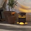 Dekoracyjna solarna lampa ogrodowa LED z możliwością ładowania USB, emitująca ciepłe światło, ustawiona obok donic z roślinami na tarasie.