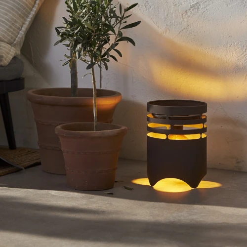 Dekoracyjna solarna lampa ogrodowa LED z możliwością ładowania USB, emitująca ciepłe światło, ustawiona obok donic z roślinami na tarasie.