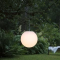 Solarna lampa ogrodowa LED w kształcie kuli zawieszona na gałęzi drzewa, emituje ciepłe światło i tworzy nastrojową atmosferę w ogrodzie.