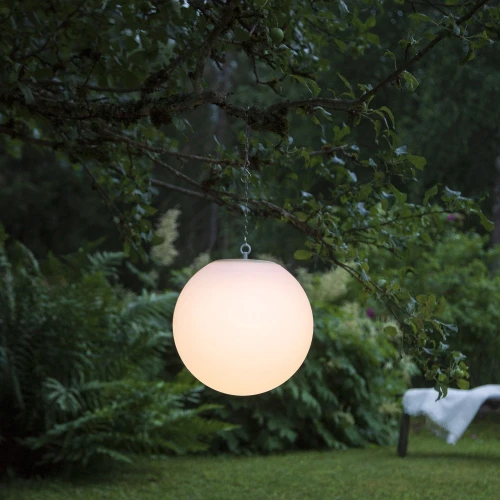 Solarna lampa ogrodowa LED w kształcie kuli zawieszona na gałęzi drzewa, emituje ciepłe światło i tworzy nastrojową atmosferę w ogrodzie.
