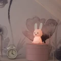 Lampka nocna króliczek z ciepłym, subtelnym światłem, umieszczona na półce jako dekoracyjne i spokojne źródło światła do zasypiania.