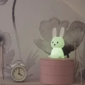 Lampka nocna króliczek świecąca jasnym zielonym światłem, stojąca na komodzie jako delikatne oświetlenie do wieczornego relaksu.