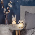 Lampka nocna króliczek oraz lampka w kształcie sowy na stoliku nocnym, tworzące przytulne i ciepłe oświetlenie sypialni.