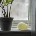 Lampka nocna w formie wieloryba ustawiona przy oknie, emitująca ciepłe, żółtawe światło.