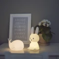 Lampki nocne wieloryb i króliczek ustawione obok siebie na komodzie, świecące ciepłym światłem w spokojnej aranżacji sypialni.