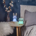 Lampki nocne w kształcie króliczka i sowy z chłodnym, niebiesko-zielonym światłem, ustawione na stoliku przy łóżku, tworzą spokojny i relaksujący klimat wieczorem.