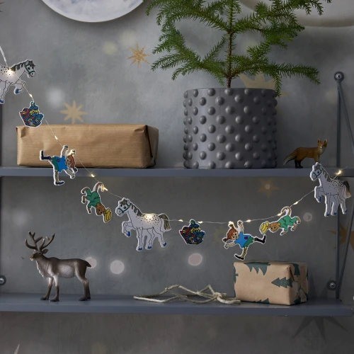 Girlanda świetlna Pippi zawieszona na półce wśród dekoracji i roślin, tworzy przytulny klimat dzięki ciepłemu światłu LED i kolorowym zawieszkom.