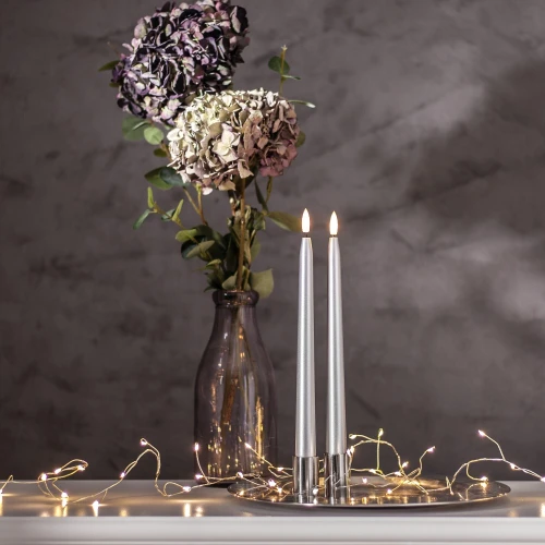Srebrne świece LED ustawione na tacy obok wazonu z hortensjami, tworzą spokojną i elegancką dekorację z delikatnym światłem.