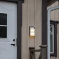 Kinkiet solarny zamontowany przy wejściu do domu, emituje ciepłe białe światło i subtelnie podkreśla elewację, zapewniając funkcjonalne oświetlenie strefy drzwi po zmroku.