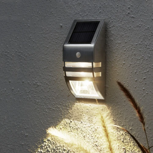 Solarny kinkiet z czujnikiem ruchu zamontowany na elewacji oświetla przestrzeń przy ścianie, zapewniając wygodę i lepszą widoczność po zmroku.