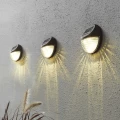 Lampy solarne zamontowane na elewacji, ustawione w rzędzie, delikatnie podkreślające strukturę ściany i tworzące dekoracyjny efekt świetlny po zmroku.