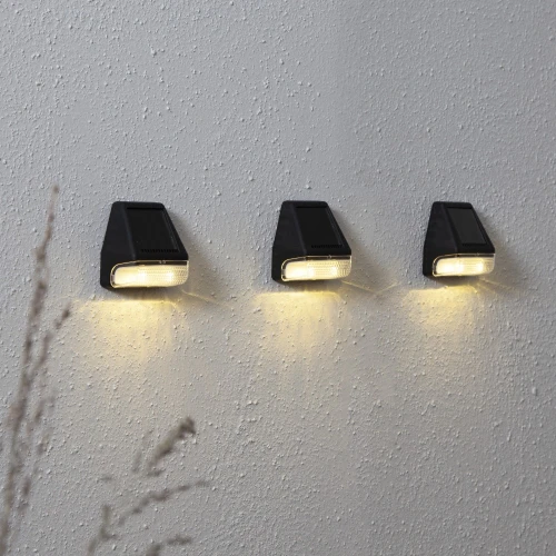Trzy lampy solarne LED zamontowane na ścianie, emitujące ciepłe światło skierowane w dół, idealne do oświetlenia elewacji lub ogrodu.