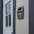 Solarna lampa z podświetlanym numerem domu „12d”, zamontowana na elewacji obok drzwi wejściowych.