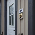 Solarna lampa z numerem „12d” zamontowana na elewacji obok drzwi, ułatwiająca odnalezienie adresu po zmroku.