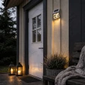 Lampa solarna z numerem domu zamontowana przy wejściu, delikatnie podświetla ścianę i oznaczenie adresu po zmroku.