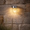 Solarny kinkiet ogrodowy LED z czujnikiem ruchu zamontowany na kamiennej ścianie tworzy efektowne rozproszone światło wokół lampy.