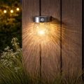 Solarny kinkiet ogrodowy LED z czujnikiem ruchu na drewnianej ścianie tworzy dekoracyjne rozproszone światło w przestrzeni ogrodu lub przy tarasie.