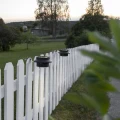Solarne lampy LED montowane na ogrodzeniu oświetlają linię płotu i przestrzeń wokół ogrodu zapewniając praktyczne doświetlenie po zmroku.