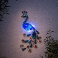 Lampa ścienna solarna w formie pawia z delikatnym podświetleniem i ozdobnymi detalami, idealna do stworzenia przytulnej atmosfery w ogrodzie lub na patio.