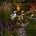 Dekoracyjna czapla ogrodowa z ażurowymi skrzydłami subtelnie rozświetla wieczorną aranżację, podkreślając ścieżkę i rośliny ciepłym, nastrojowym światłem.