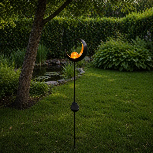 Solarna lampa ogrodowa w formie półksiężyca z dekoracyjną kulą LED, ustawiona na trawniku wśród zieleni. Ciepłe światło subtelnie podkreśla rośliny i wprowadza spokojny, wieczorny klimat.