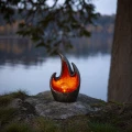 Dekoracyjna lampa solarna LED w formie płomienia ustawiona na kamieniu nad brzegiem jeziora. Ciepłe, bursztynowe światło tworzy spokojny, nastrojowy klimat i subtelnie podkreśla naturalne otoczenie.
