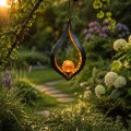 Wisząca lampa solarna LED w formie płomienia z dekoracyjną kulą, zawieszona wśród zieleni nad ogrodową ścieżką. Ciepłe światło tworzy przyjemny nastrój i subtelnie podkreśla naturalny charakter przestrzeni.