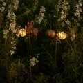 Oświetlone dekoracje w kształcie muchy i mrówki wśród kwiatów, ciepłe światło LED tworzy przytulny klimat po zmroku.