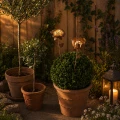 Solarne lampy w kształcie kwiatów umieszczone w donicy z kulistą rośliną, delikatnie oświetlają przestrzeń i dodają przytulnego charakteru tarasowi po zmroku.