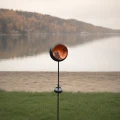 Solarny lampion ogrodowy z motywem wróżki i gwiazdy w okrągłej oprawie, emitujący ciepłe światło LED, ustawiony przy jeziorze, jako dekoracyjne oświetlenie przestrzeni zewnętrznej i strefy wypoczynku.