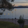 Solarne lampki ogrodowe LED w kształcie dmuchawców rozmieszczone przy brzegu jeziora. Dekoracyjne światło subtelnie podkreśla naturalny krajobraz i nadaje przestrzeni wyjątkowy, relaksujący charakter.
