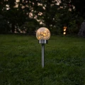 Solarna lampa ogrodowa LED w formie szklanej kuli z efektem spękanego szkła umieszczona na trawniku, emitująca ciepłe światło, dekoracyjne oświetlenie do ogrodu i wzdłuż ścieżek.