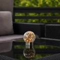 Dekoracyjna lampa solarna LED w kształcie szklanej kuli z efektem spękanego szkła ustawiona na stole tarasowym, emitująca ciepłe światło, eleganckie oświetlenie na balkon, taras i do ogrodu.