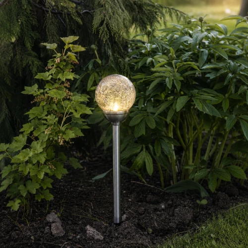 Solarna lampa ogrodowa LED w formie świecącej szklanej kuli umieszczona wśród roślin, dekoracyjne oświetlenie zewnętrzne z ciepłym światłem do ogrodu i na taras.