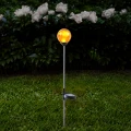 Solarna lampa ogrodowa LED z bursztynową kulą emitującą ciepłe światło ustawiona na trawniku, eleganckie oświetlenie zewnętrzne do ogrodu, rabat i ścieżek.