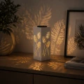Dekoracyjny lampion solarny LED z ażurowym wzorem liści ustawiony na komodzie, emitujący ciepłe światło i tworzący przytulny klimat we wnętrzu.