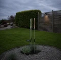 Solarne lampy ogrodowe LED z kolorowym efektem świetlnym ustawione na kamiennej rabacie przy drewnianym ogrodzeniu.