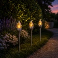 Dekoracyjne lampy solarne LED z efektem płomienia oświetlające rabatę i ścieżkę ogrodową po zmroku.