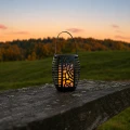 Solarna lampa ogrodowa LED z efektem płomienia ustawiona na drewnianej barierce o zachodzie słońca.