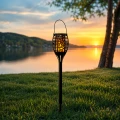 Solarna lampa LED z efektem płomienia ustawiona nad jeziorem podczas zachodu słońca.
