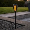 Solarna lampa ogrodowa LED z ciepłym światłem umieszczona przy żwirowej rabacie i nowoczesnej aranżacji ogrodu.