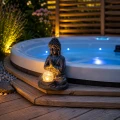 Solarna dekoracja ogrodowa Buddha LED ustawiona przy jacuzzi na drewnianym tarasie, emitująca ciepłe światło po zmroku.