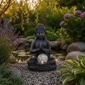 Solarna figurka Buddha LED z dekoracyjną szklaną kulą emitującą ciepłe światło w ogrodzie przy oczku wodnym.